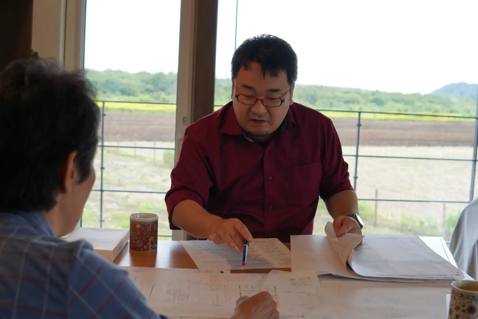 大きな窓の前で図面を広げた住まい手との対話